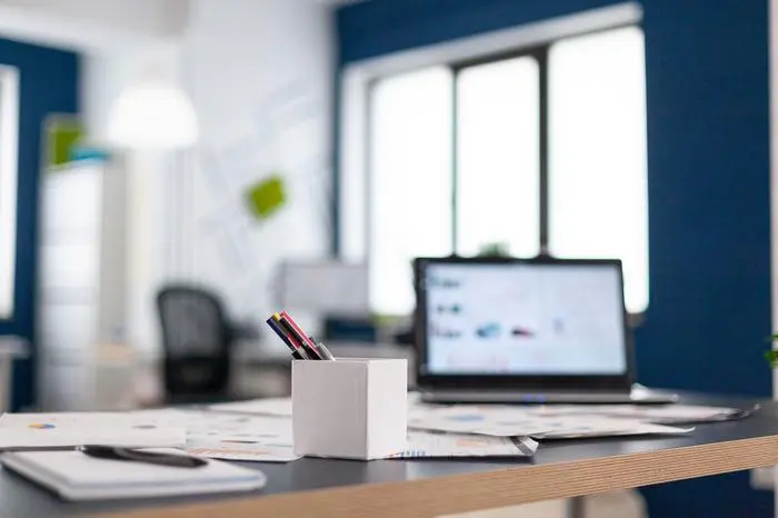 Laptop with company financial charts on office desk. Brainstorm area in business center with nobody in it, shot of empty room with modern furniture and blue wall.
