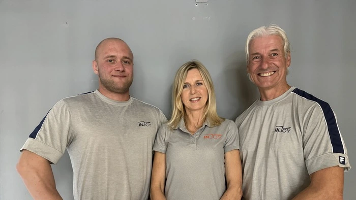Das Bild zeigt zwei trainierte Männer und eine Frau in grauen Injoy-Shirts und schwarzer Trainingshose.
