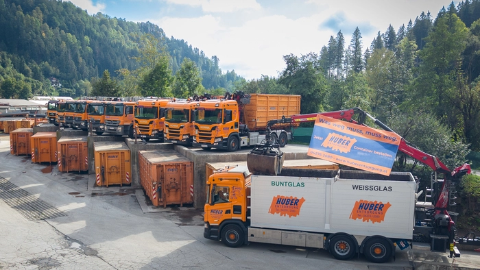 Das Bild zeigt orange Lkw und Container mit dem Logo „Huber Entsorgung“