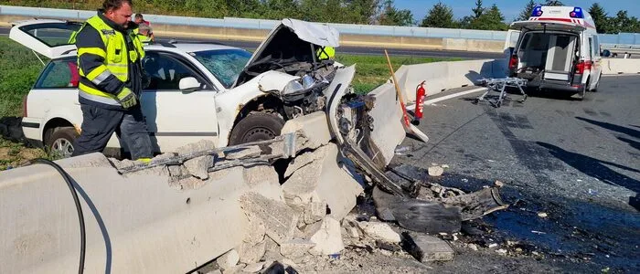Ein weißer Pkw mit zerstörter Front steht an einer zerschmetterten Betonleitwand