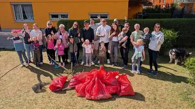Eine Gruppe von rund 25 Kindern und Erwachsenen steht hinter einem Berg gefüllter, roter Müllsäcke