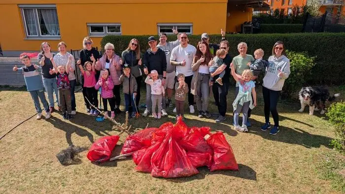 Eine Gruppe von rund 25 Kindern und Erwachsenen steht hinter einem Berg gefüllter, roter Müllsäcke