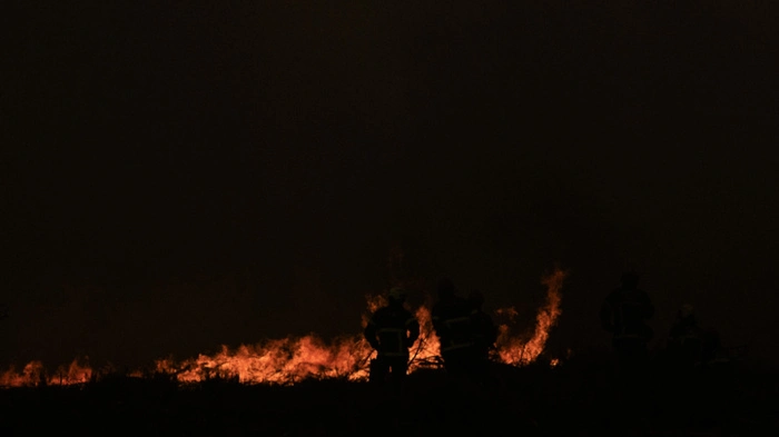 Firefighters spray water along the edge of a forest during a wildfire near the town of Lege-Cap-Ferret, southwestern France on July 25, 2026. Fires are raging on July 25, 2026 in France and Spain, with nearly 260,000 people evacuated near the big French city of Bordeaux and in the Madrid region, a metropolis confronted with the "worst" fire in its history. Scientists have long warned that climate change caused by human use of fossil fuels will make periods of drought more intense and longer-lasting, creating the ideal conditions for wildfires. (Photo by JULIEN DE ROSA / AFP)