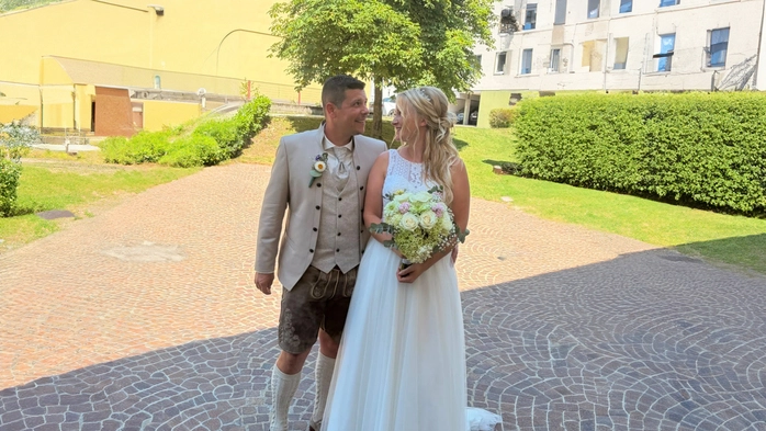 Die Brautleute Jasmin und Christian Bierbaumer nach der standesamtlichen Trauung. Sie trägt ein weißes ärmelloses Kleid, er Tracht und Lederhose.