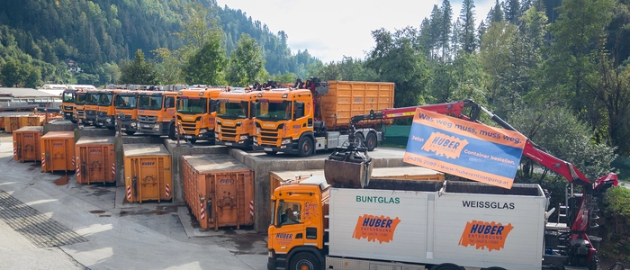 Das Bild zeigt orange Lkw und Container mit dem Logo „Huber Entsorgung“