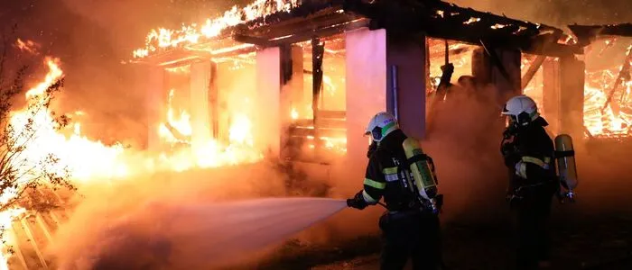 Zwei Feuerwehrleute gehen mit Löschschlauch gegen ein in Flammen stehendes Gebäude vor