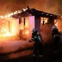 Zwei Feuerwehrleute gehen mit Löschschlauch gegen ein in Flammen stehendes Gebäude vor