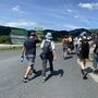 Eine Gruppe Wanderer geht eine Straße entlang, man sieht alle nur von hinten