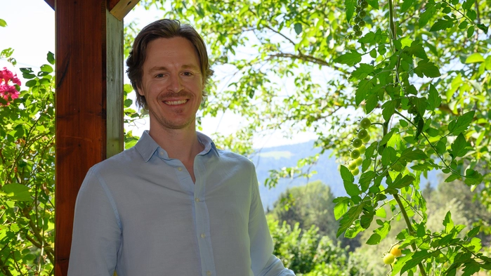Lied- und Opernsänger Georg Klimbacher steht auf der Terrasse seines Elternhauses mit Blick ins Grüne. Er trägt ein blaues lockeres Leinenhemd:
