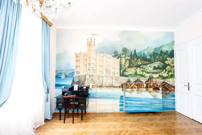 Hinter einer "Tapetentür" einer Wand, die das Schloss Miramare bei Triest zeigt, verstecken sich die Sanitärräume.