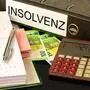 Zwei Mappen – eine mit der Rückenaufschrift „Insolvenz“ –, Geldscheine und ein Taschenrechner