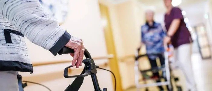 Senioren mit Rollator und eine Pflegekraft in einem Pflegeheim zu sehen (Sujet)