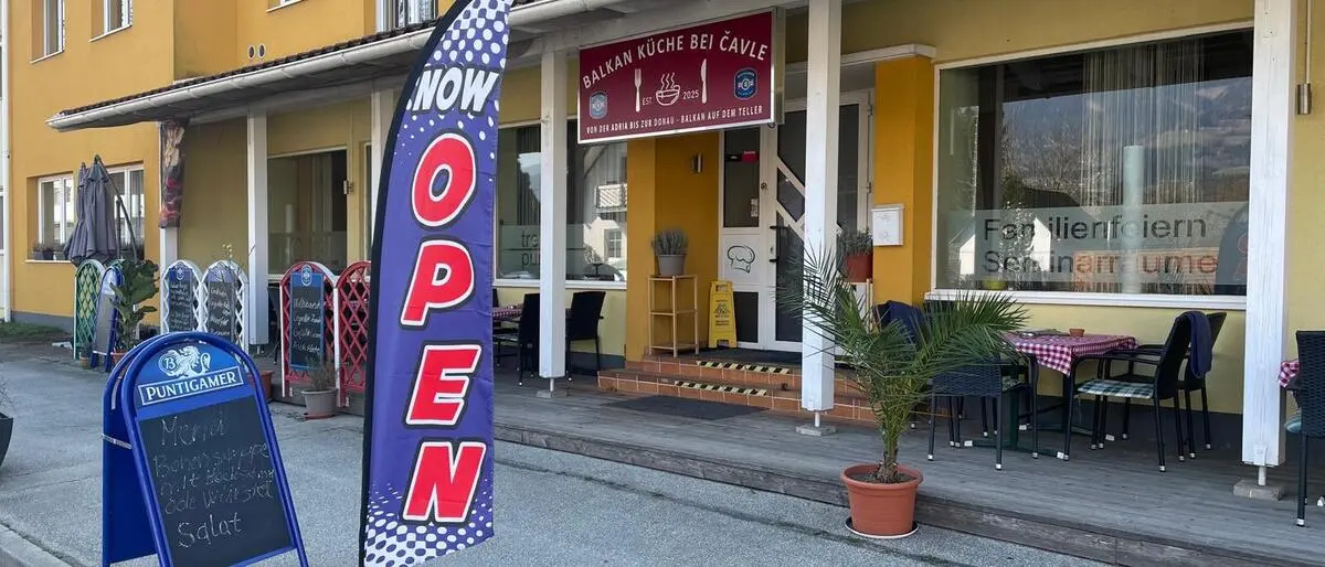 Ein gelbes Gebäude mit einer rot-weißen Fahne, worauf „geöffnet“ steht