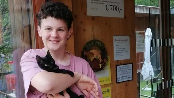 Ein Junge steht mit einer Katze am Arm vor dem Tierheim