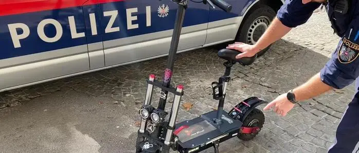 Polizist mit einem E-Scooter vor einem Polizeiauto