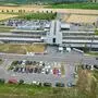 Zu sehen ist ein Bahnhof aus der Vogelperspektive, einige Autos parken in der Wiese 