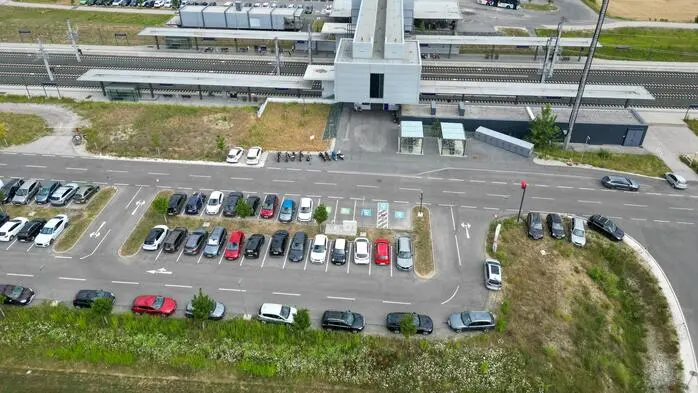 Zu sehen ist ein Bahnhof aus der Vogelperspektive, einige Autos parken in der Wiese 