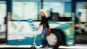 Eine Frau fährt auf einem E-Scooter vor einem Linienbus vorbei