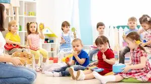 Eine Gruppe Kindergartenkinder sitzt mit Musikinstrumenten in den Händen im Halbkreis am Boden um eine Betreuerin