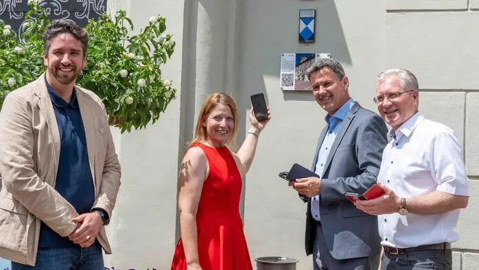Drei Männer und eine Frau lächeln bei sonnigem Wetter in die Kamera.