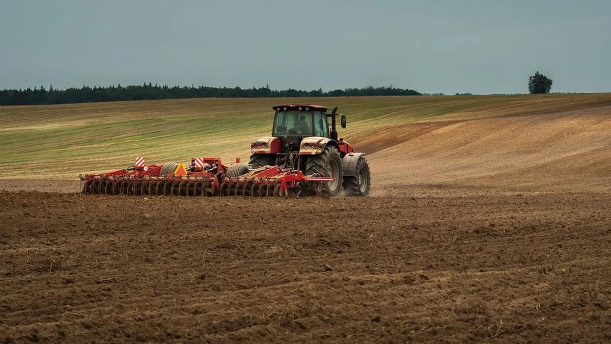 agricultural industrial landscape. a modern tractor with a trailed cultivator works on a wide hilly field before the autumn sowing campaign
