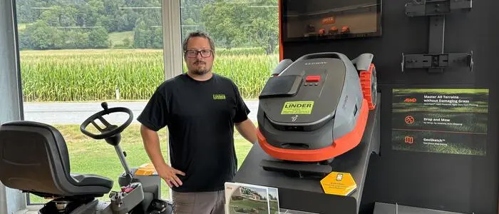 Ein Mann steht neben einem Rasenmäherroboter. Neben ihm befindet sich ein Mähtraktor.