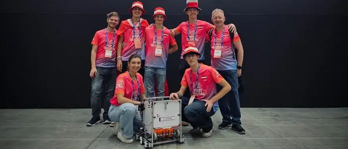 Mehrere Personen im gleichen T-Shirt und teilweise mit rot-weiß-roten Hüten stehen vor einer Wand, auf der „First Global“ steht