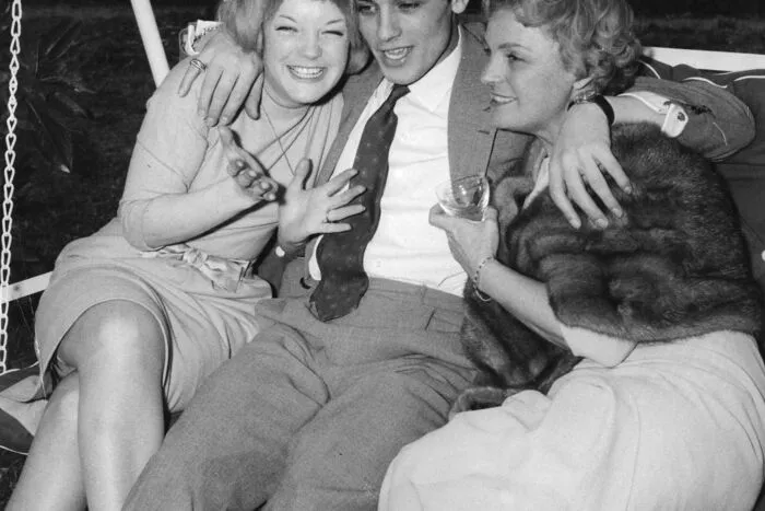 Romy Schneider sitzt am 22. Maerz 1959 mit ihrer Mutter Magda, rechts, und dem franzoesischen Schauspieler Alain Delon in einer Hollywood-Schaukel in Morcote bei Lugano, Schweiz.