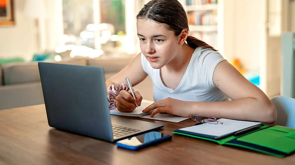 Teenager girl studying online at home looking at laptop at  quarantine isolation period during pandemic. Home schooling. Social distancing. Online school test.