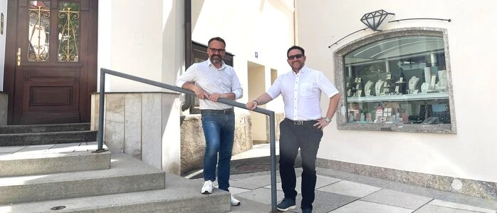 Zwei Männer mit weißen Hemden stehen vor ihren Geschäftslokalen