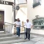 Zwei Männer mit weißen Hemden stehen vor ihren Geschäftslokalen 