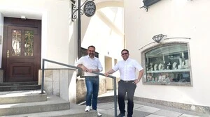 Zwei Männer mit weißen Hemden stehen vor ihren Geschäftslokalen 