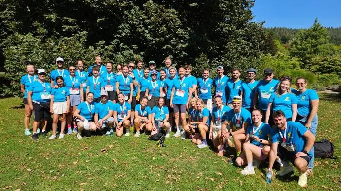 Eine große Gruppe Sportlerinnen und Sportler in blauen T-Shirts steht auf einer Wiese