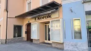 Die Vorderansicht eines Geschäftes in einem Haus in einem hellen Pastell-Orange, das leer steht. Der Name des Geschäftes steht über dem Eingang - F. Korak | Im Korak-Haus entsteht das „Bacaro“ am Völkermarkter Hauptplatz