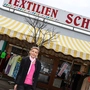 Eine blonde Dame steht vor ihrem Geschäft mit der Aufschrift „Textilien Schmid“