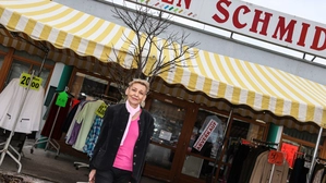 Eine blonde Dame steht vor ihrem Geschäft mit der Aufschrift „Textilien Schmid“