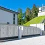 Seitlicher Blick auf weiße Batteriespeicherkästen, am Hügel dahinter steht ein kraftwerkähnliches Gebäude