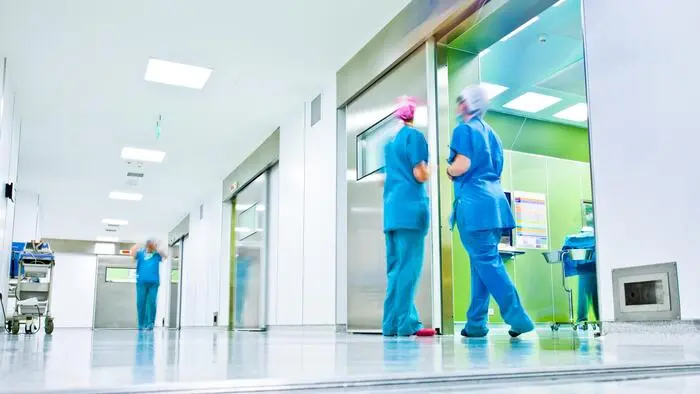 Mitarbeiter in blauer Kleidung mit Kopfbedeckung in einem Gang eines Krankenhauses | Die Versetzung einer Betriebsrätin sorgt innerhalb der Kabeg für hitzige Debatten (Symbolfoto)