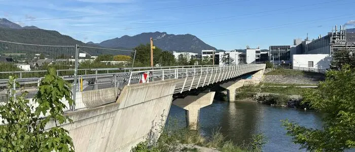 Seitlicher Blick auf eine Brücke mit Baustellengitter, im Hintergrund sanfte Berge