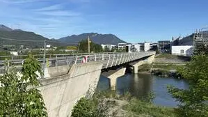 Seitlicher Blick auf eine Brücke mit Baustellengitter, im Hintergrund sanfte Berge