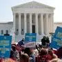 Vor den Stufen des Supreme Court sammeln sich Demonstranten, auch zahlreiche Immigranten. Sie schwenken Stars-and-Stripes-Flaggen, viele rufen „Trump must go now“