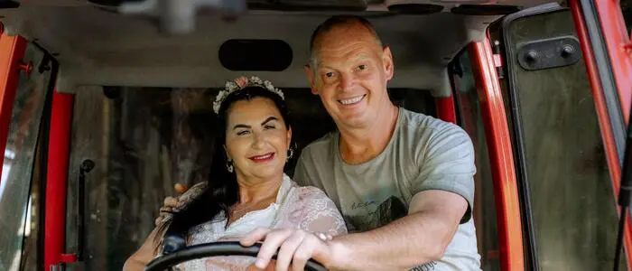 Eine Frau und ein Mann sitzen auf einem Traktor und lächeln in die Kamera.