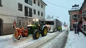 Traktor mit Schneepflug und Lkw auf Schneefahrbahn zwischen Häusern