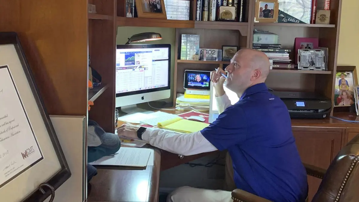 In this image provided by Jay Woods,  Woods, a Designated Market Maker with IMC and NYSE Floor Governor, who normally works on the New York Stock Exchange trading floor, works in his home office in Basking Ridge, N.J., Thursday, March 26, 2020.  Stocks are opening lower on Wall Street as the market gives back some of the gains it piled up over the past three days. (Shannon Woods/Courtesy Jay Woods via AP)