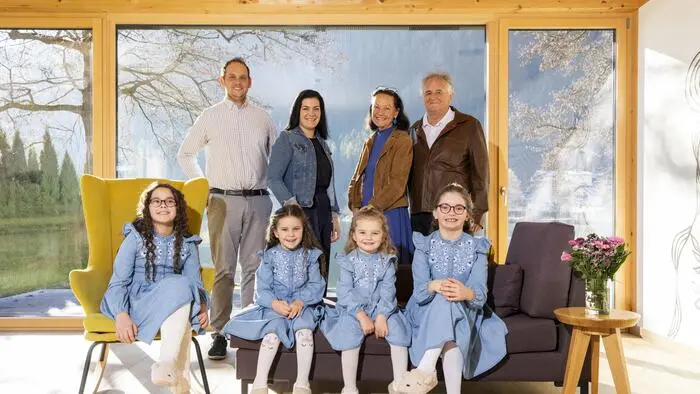 Familienfoto: in erster Reihe sitzen vier Mädchen in blauen Kleidern, dahinter stehen die Eltern und Großeltern