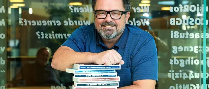 Ein Mann in einem blauen Poloshirt lehnt auf einem Stapel Bücher.