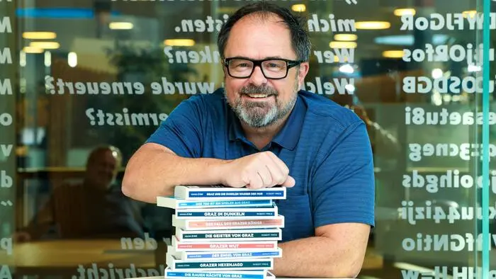 Ein Mann in einem blauen Poloshirt lehnt auf einem Stapel Bücher.