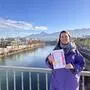 Eine Frau in violettfarbener Jacke steht auf einer Brücke und hält einen Flyer in der Hand. Im Hintergrund sieht man einen Fluss und Häuser links und rechts | Carmen Auer gründete im vergangenen Jahr ihren Verein „Woman Wonder Weibichkeit“ und organisiert jetzt ihre erste Frauenmesse