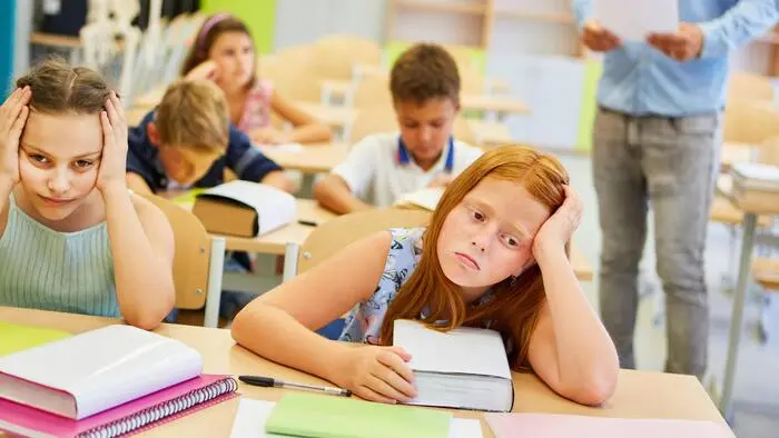 Mehrere Schülerinnen und Schüler sitzen mit erschöpftem Gesichtsausdruck in einem Klassenzimmer