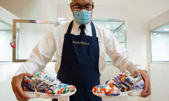 Ein Mitarbeiter von Sotheby's hält ein Paar Sneakers aus Porzellan  - eine Kooperation von  Adidas und Meissen